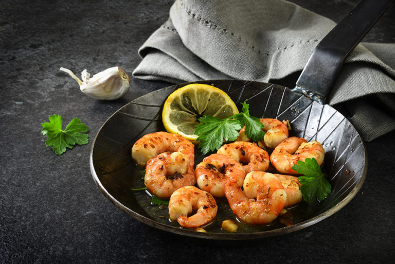 prawns shrimps with garlic, lemon, spices and italian parsley garnish in a black pan on a dark slate plate, selected focus, narrow depth of field
